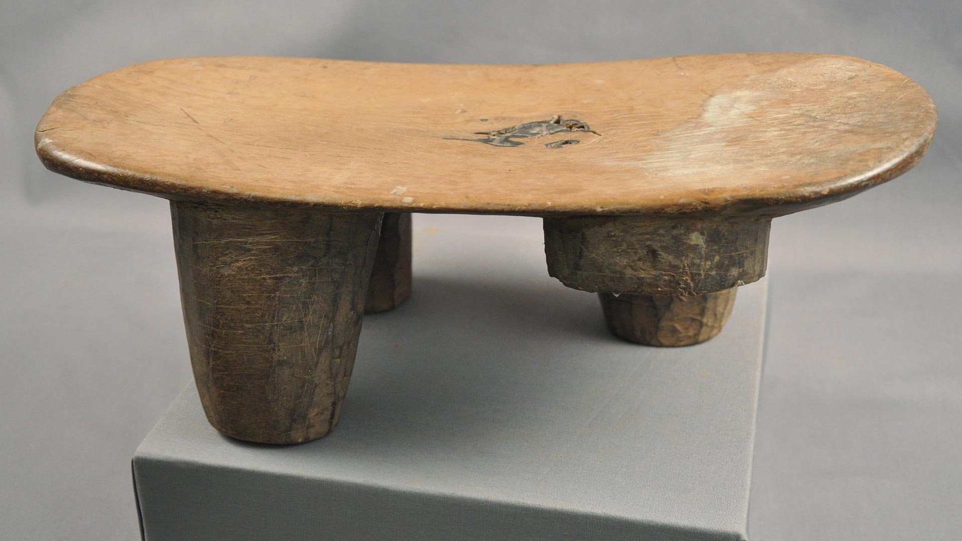 flat short wooden stool with three plain legs and a part of a fourth, broken leg
