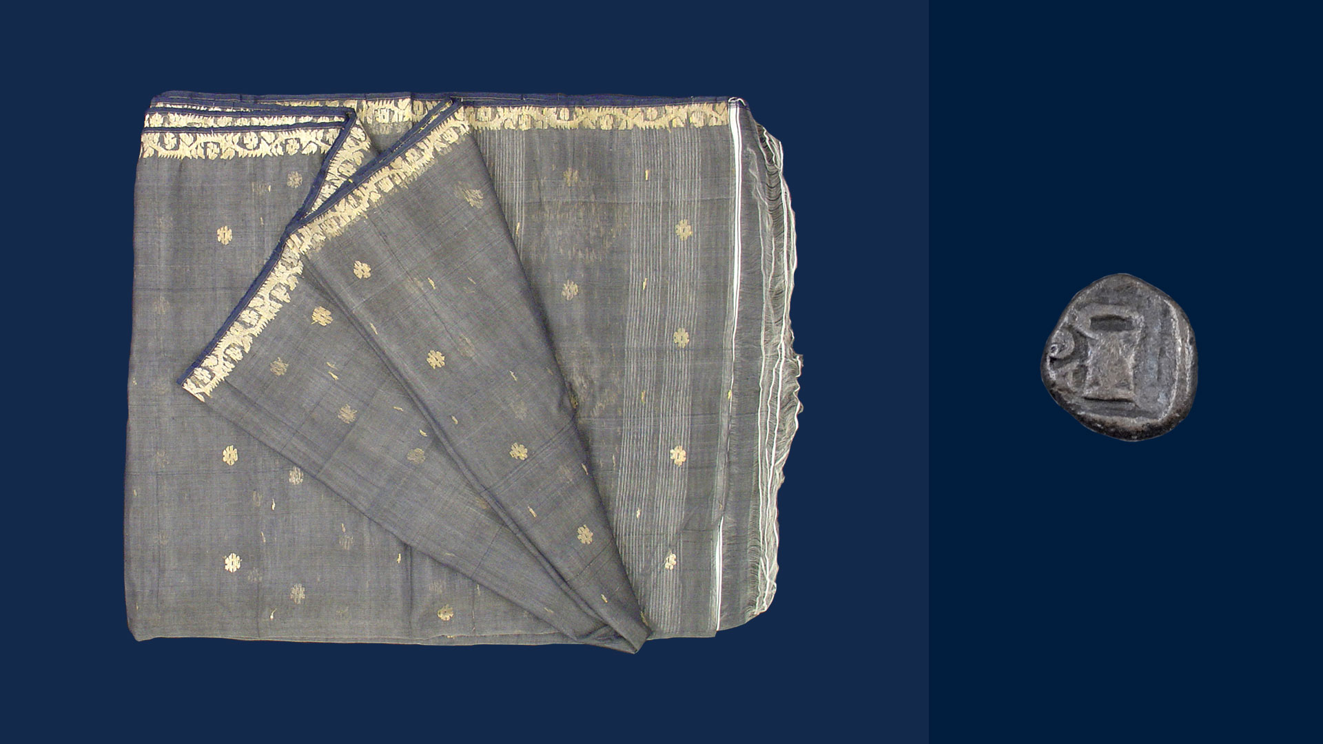 A greyish sari folded up next to a small gray coin