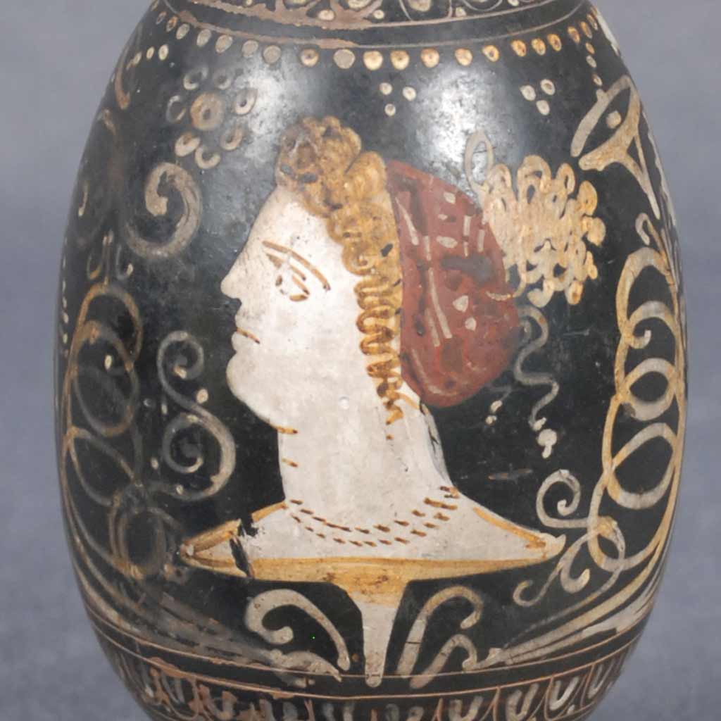 close-up of a woman's face painted on a black vase with gold decals