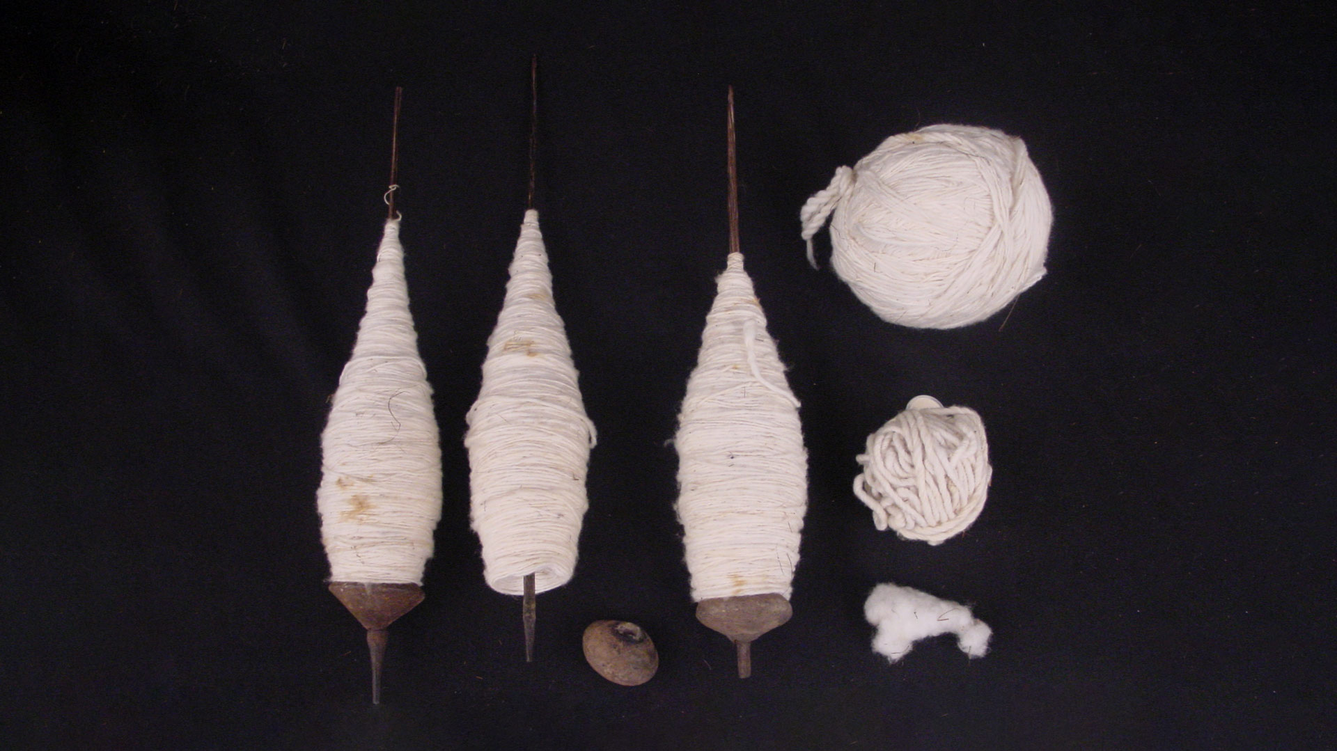 three spindles of white cotton yarn, two balls of white cotton yarn (large and small), and a small piece of white cotton fibers