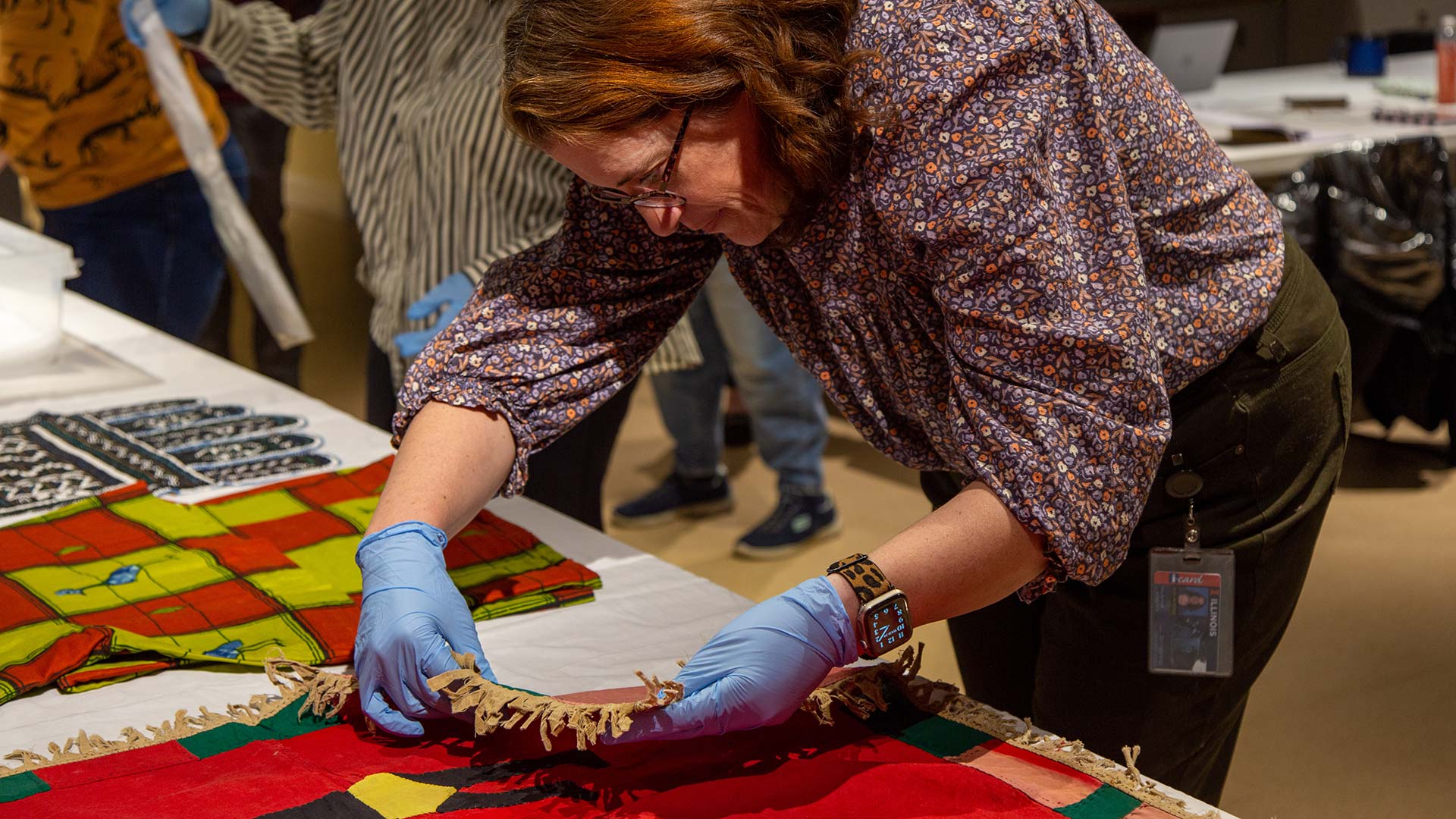 a woman carefully investigate the underside of a red textile during an artifact review