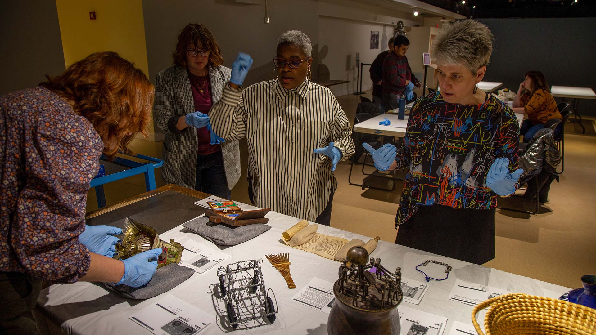 4 people with gloves discuss and examine a table of African objects inside a museum exhibit space
