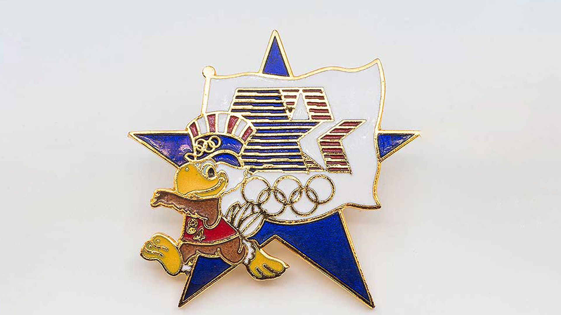 A metal pin with an eagle dressed in white, red, and blue walking on top of a star.