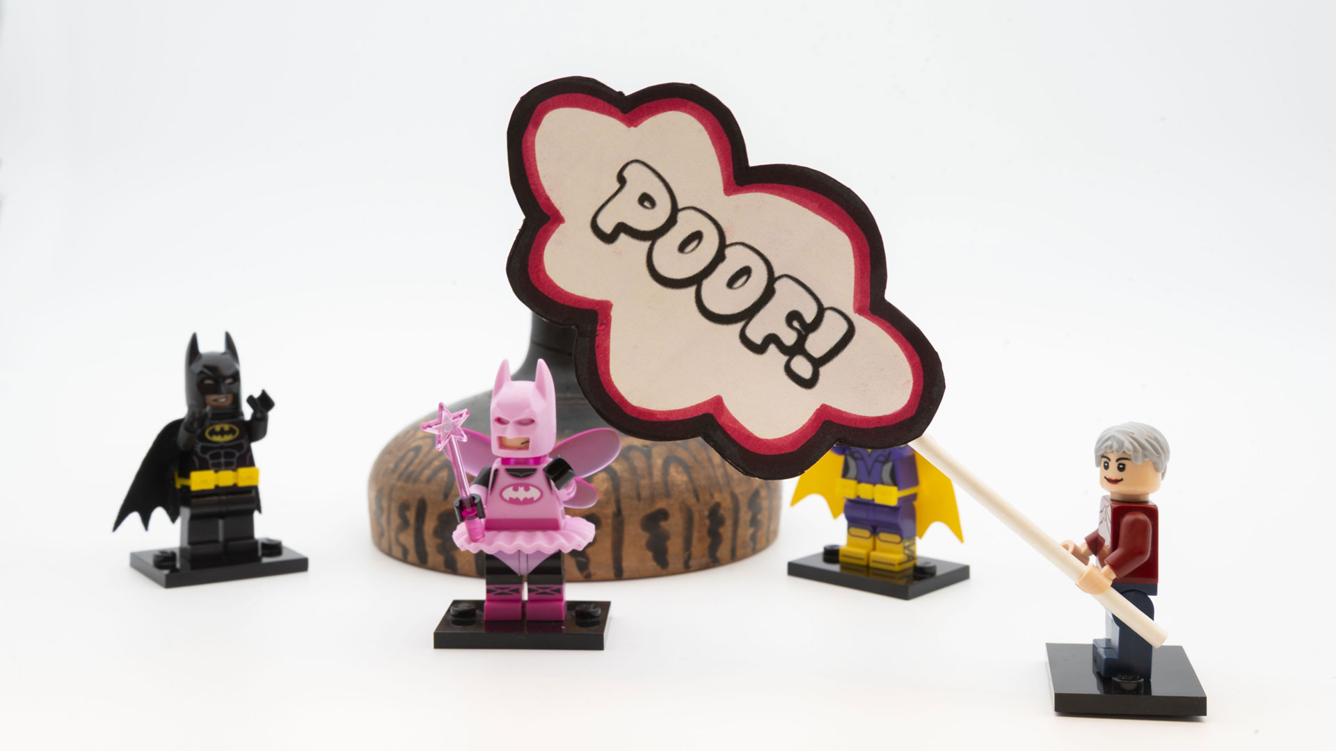 LEGO Christa holding a POOF! sign obscuring part of the repaired object as LEGO Batman and LEGO Batman Ballerina look on