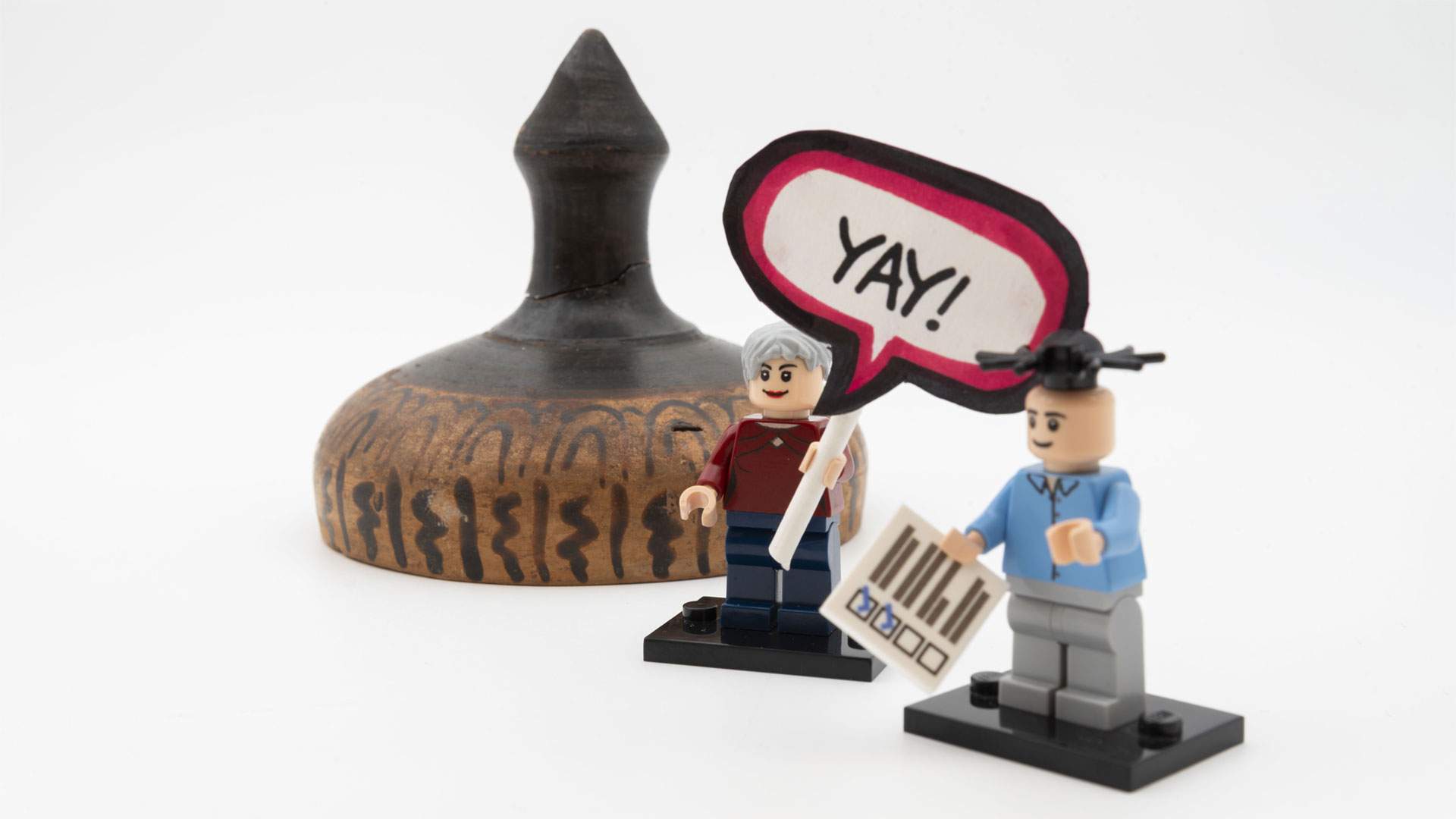 Two LEGO figures hold a YAY sign in front of a repaired object