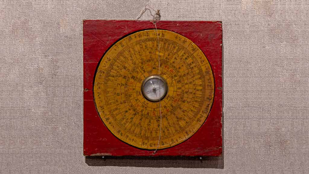 A red and orange compass with Chinese characters displayed in a circular pattern around a center of glass