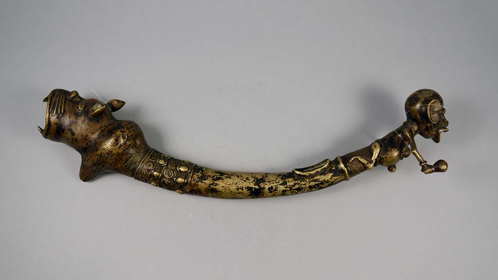 skinny, curved metal horn with a human or animal head at either end