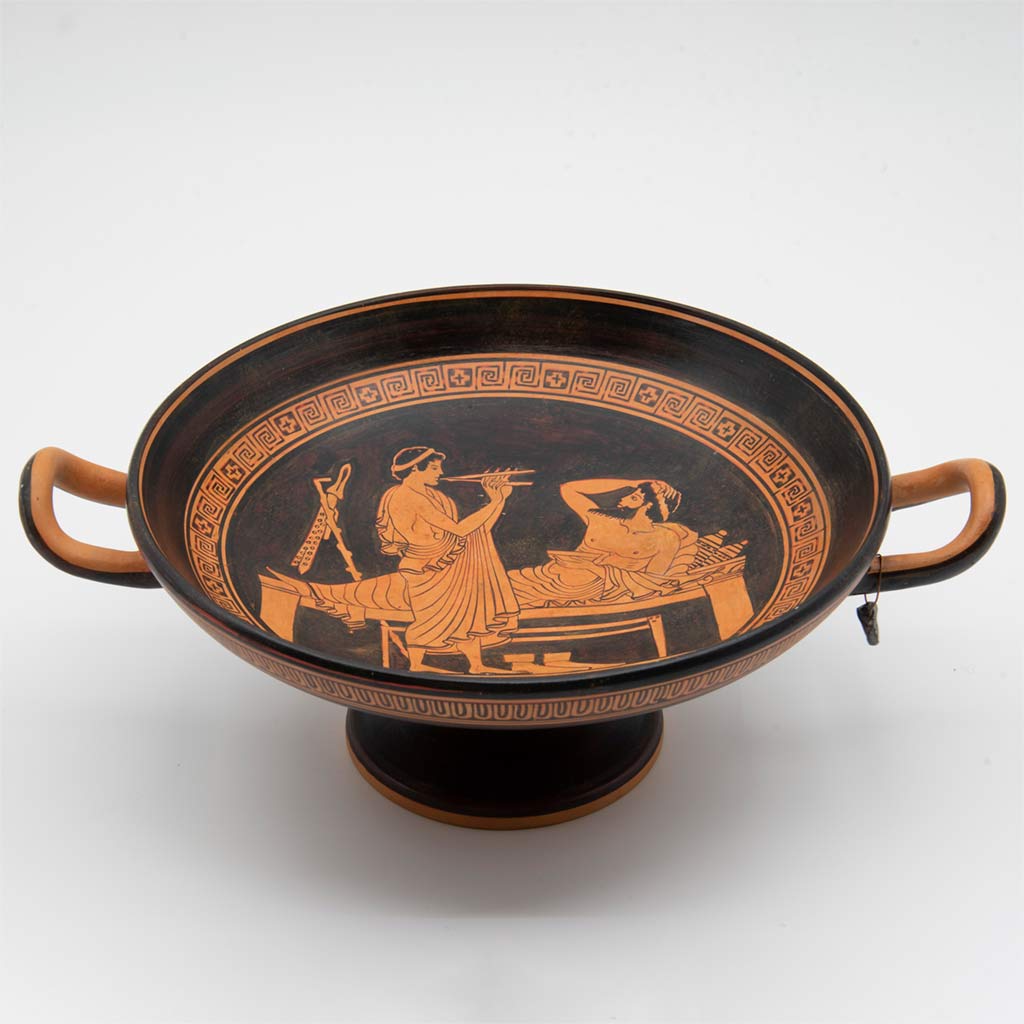 A brown and orange bowl with two handles depicting a man playing an instrument and another laying down