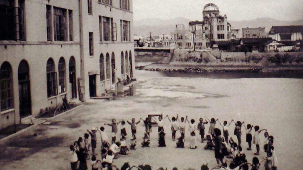Screenshot from film: children in schoolyard holding hands in a circle.