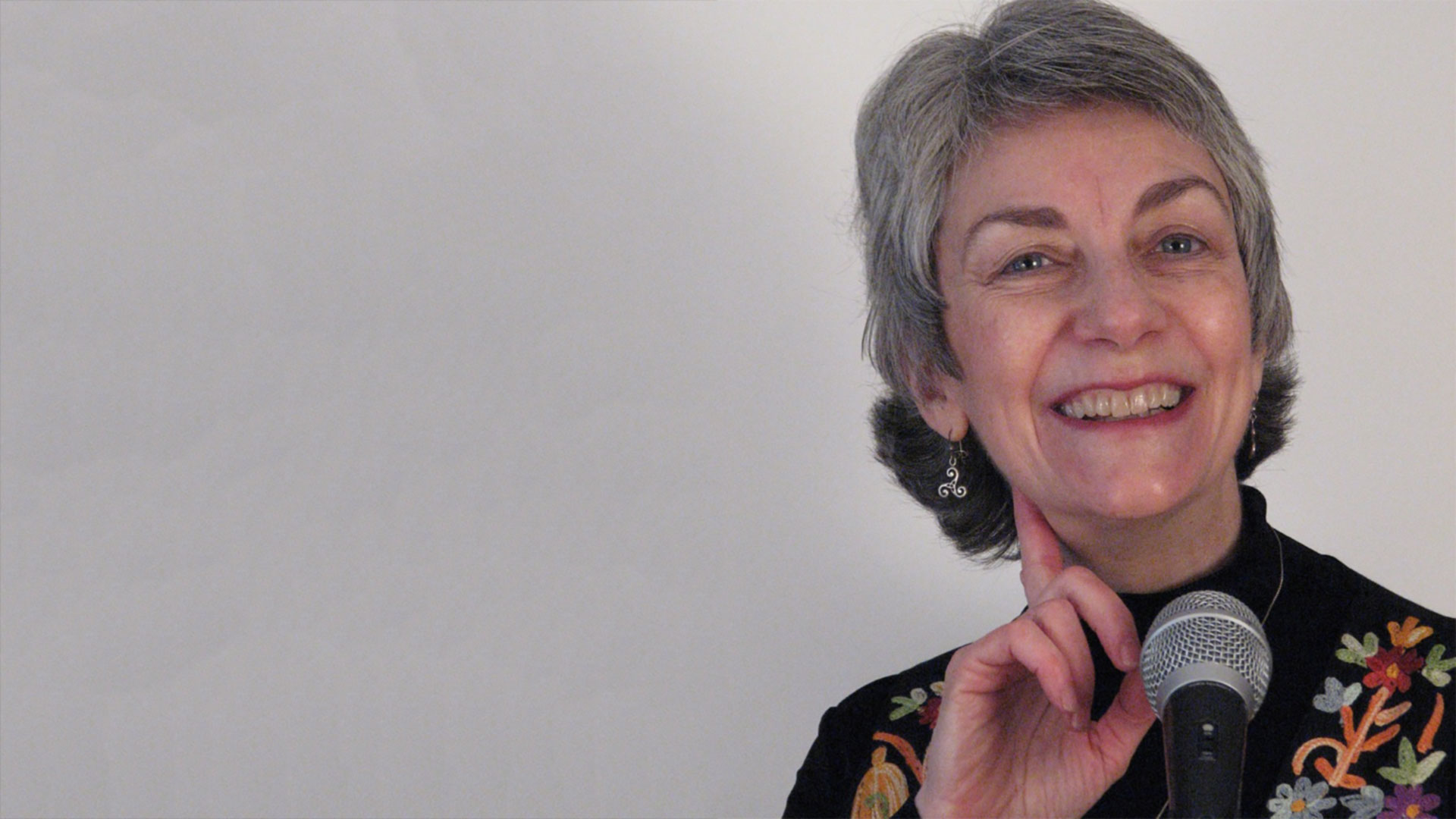 headshot of kath brinkmann smiling in front of a microphone