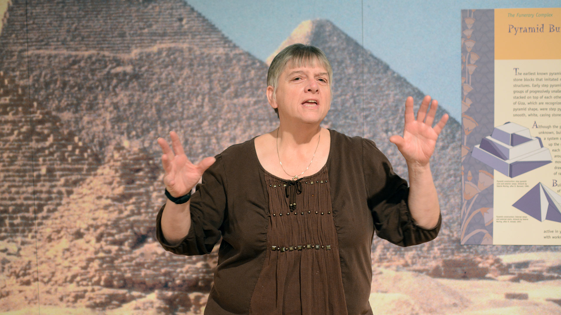woman gestures while telling stories in front of a pyramid backdrop