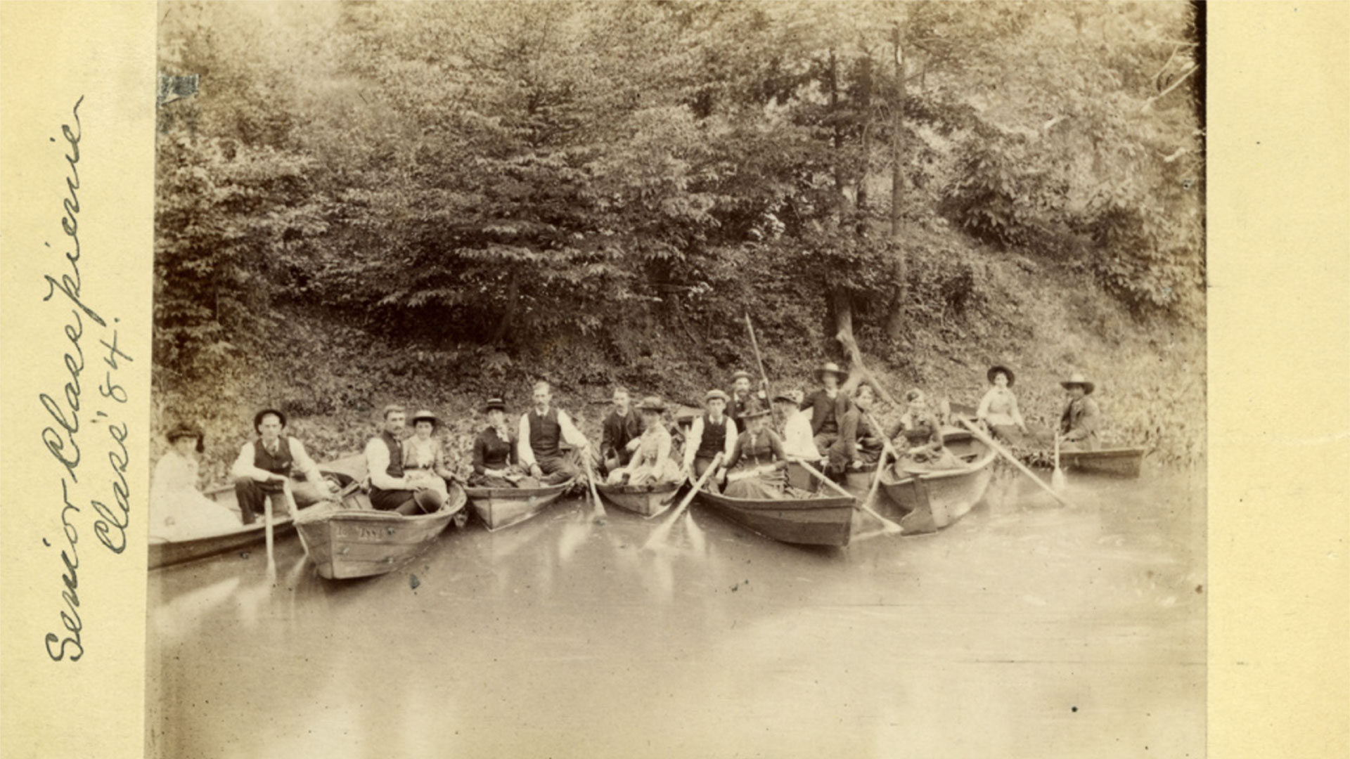 A faded picture from 1884 of many young men and women in canoes