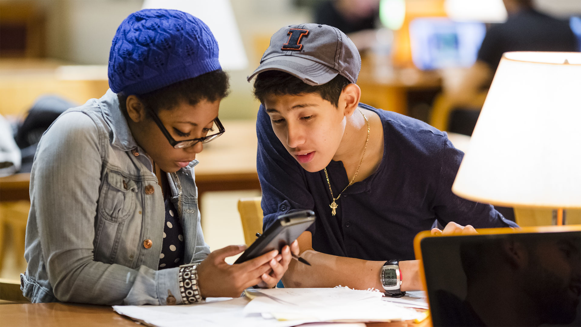 Two students study at a desk with a calculator