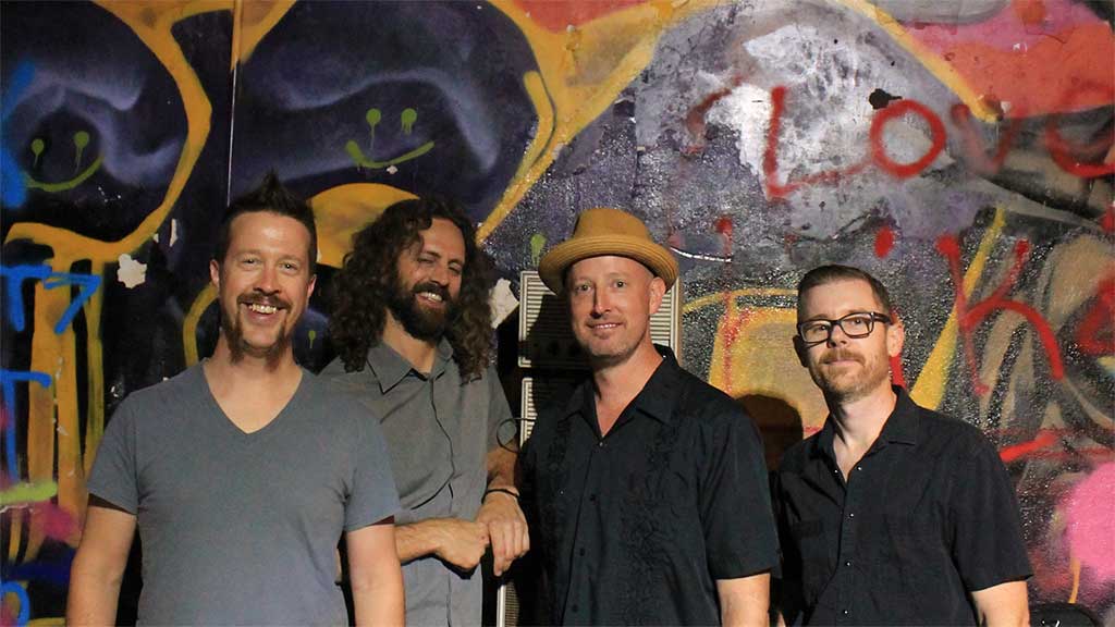 Four men, part of band Los Guapos, against a colorful graffiti wall