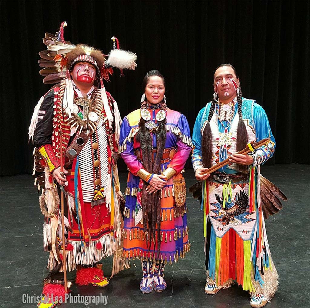 three dancers dressed in colorful clothes, one of them wearing a native traditional headgear