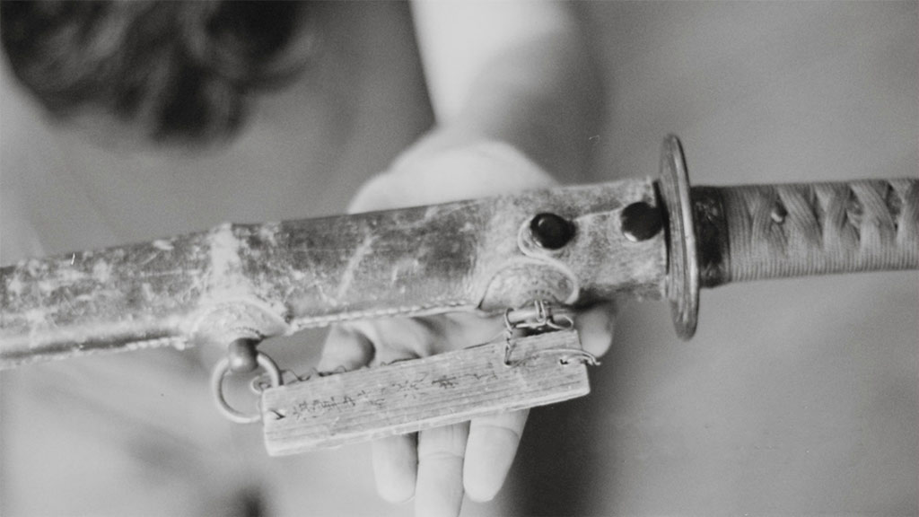 A hand is holding up a sheathed sword