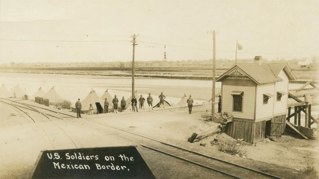 Sepia-toned photo of US soldiers on the Mexican border at the intersection of a dirt road and railroad tracks