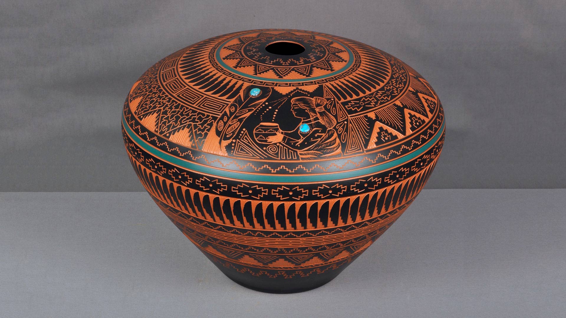 An orange clay vessel decorated with intricate black and turquoise patterns.