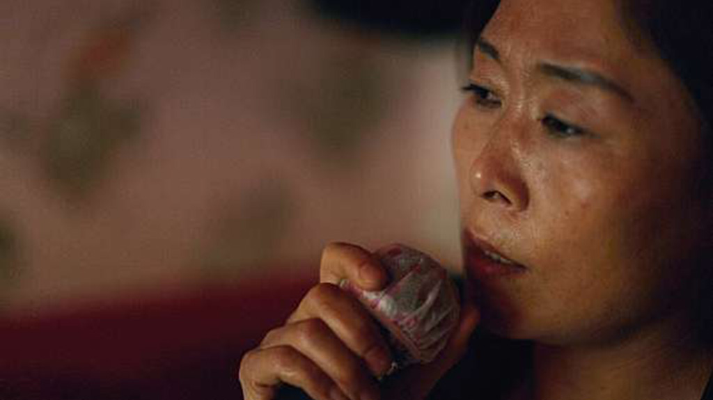 A lady holds up an object to her face as she gazes solemnly away