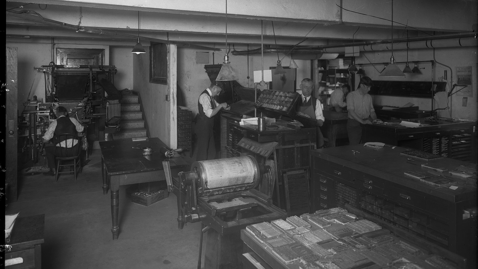 A black and white image of five men working on printing presses in an underground room