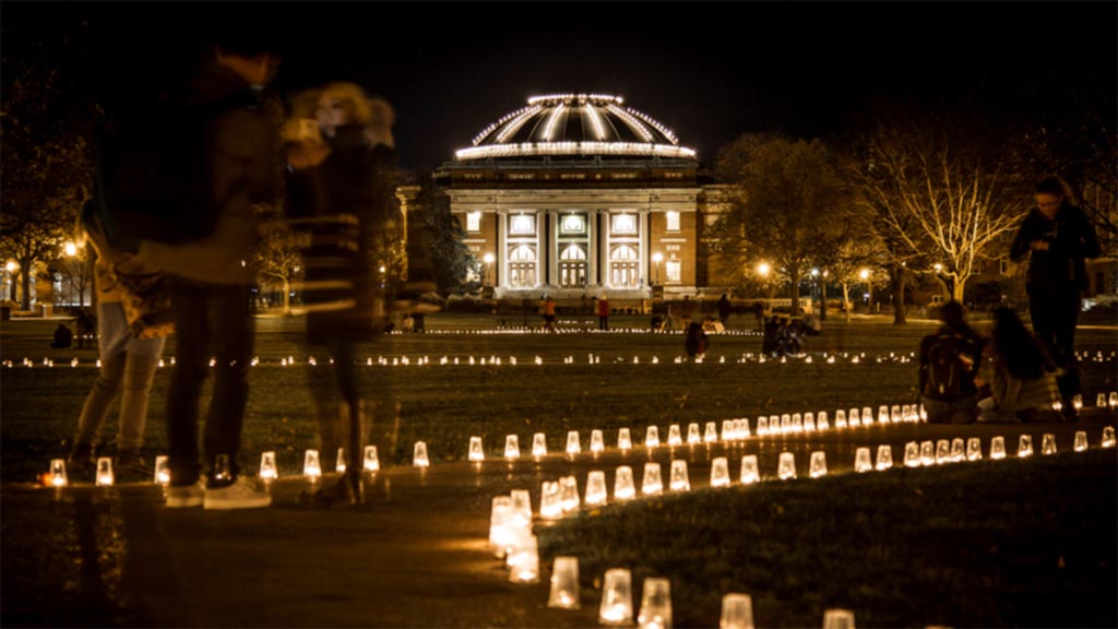 Quad at night with students gathering around luminary-lined sidewalks