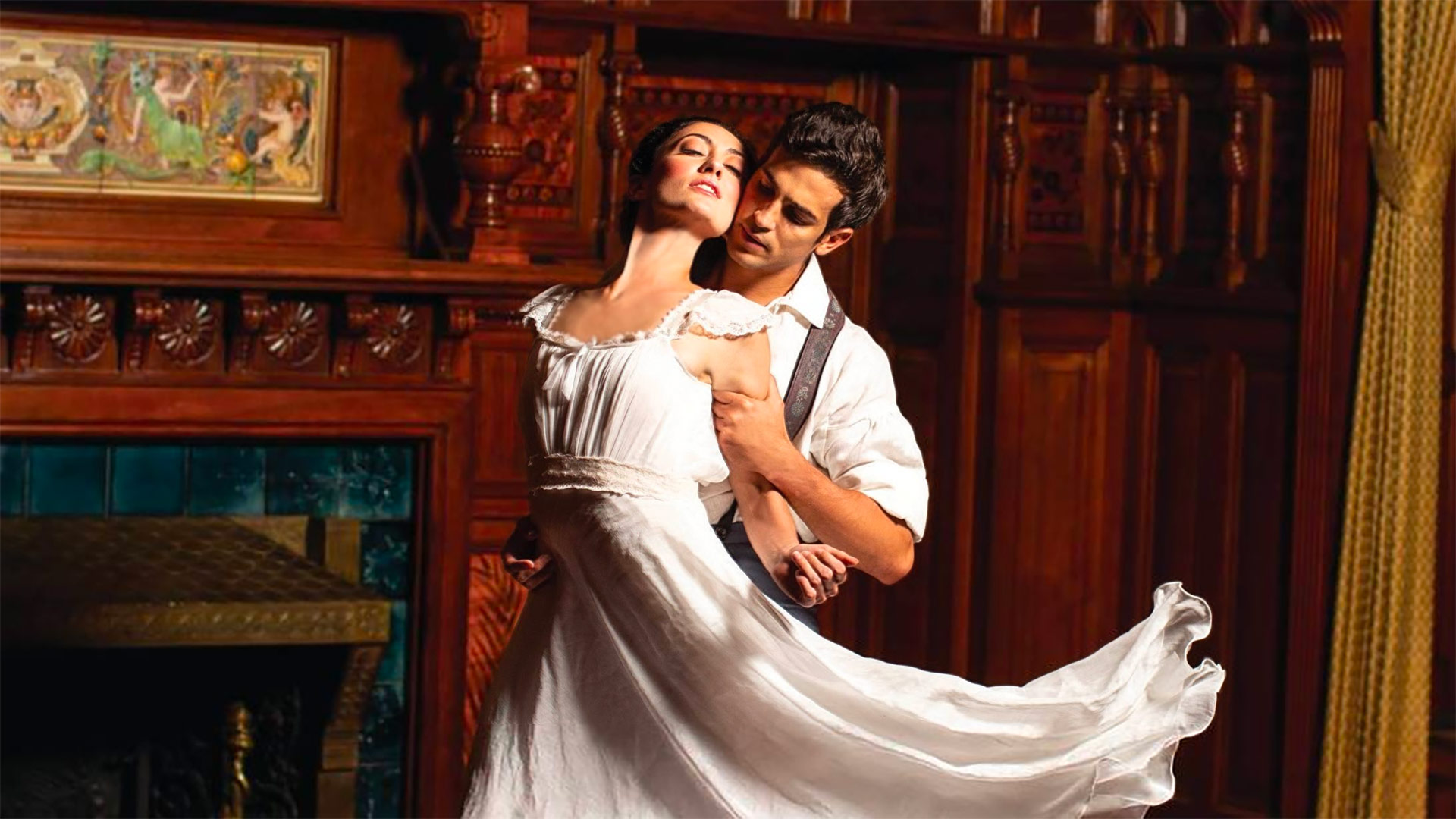 A couple in white dance in a dramatically lit mahogany-paneled room