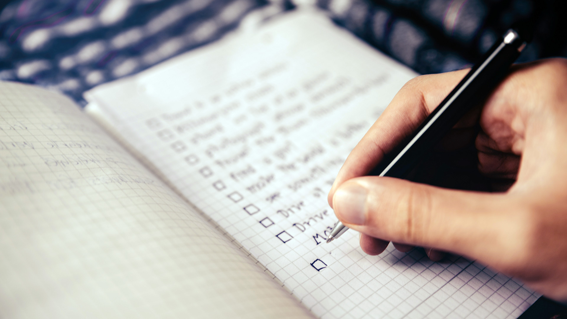 closeup of a notebook as someone writes a checklist with a pen