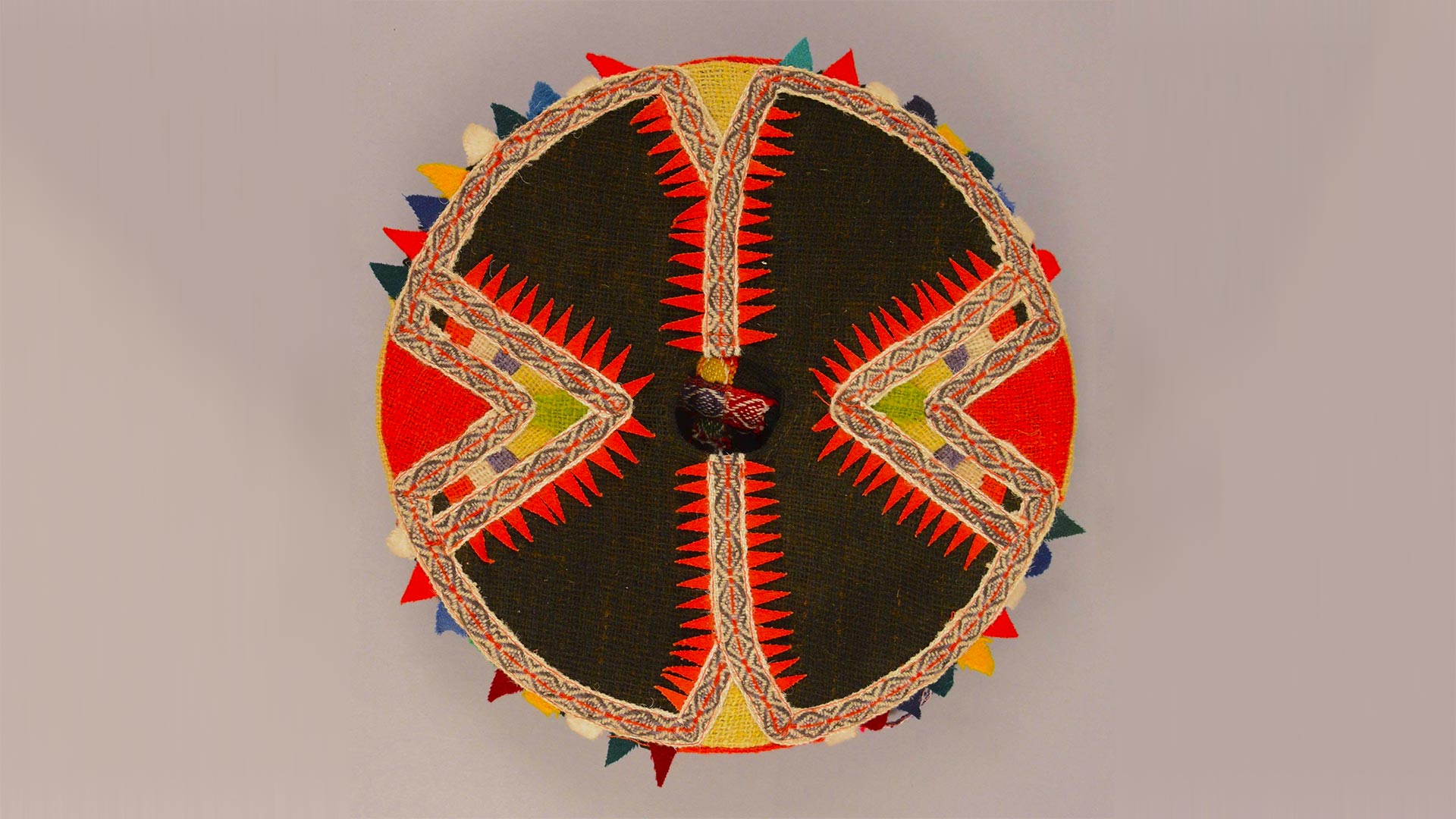 top view of a flat round woven hat with red and black pointy design