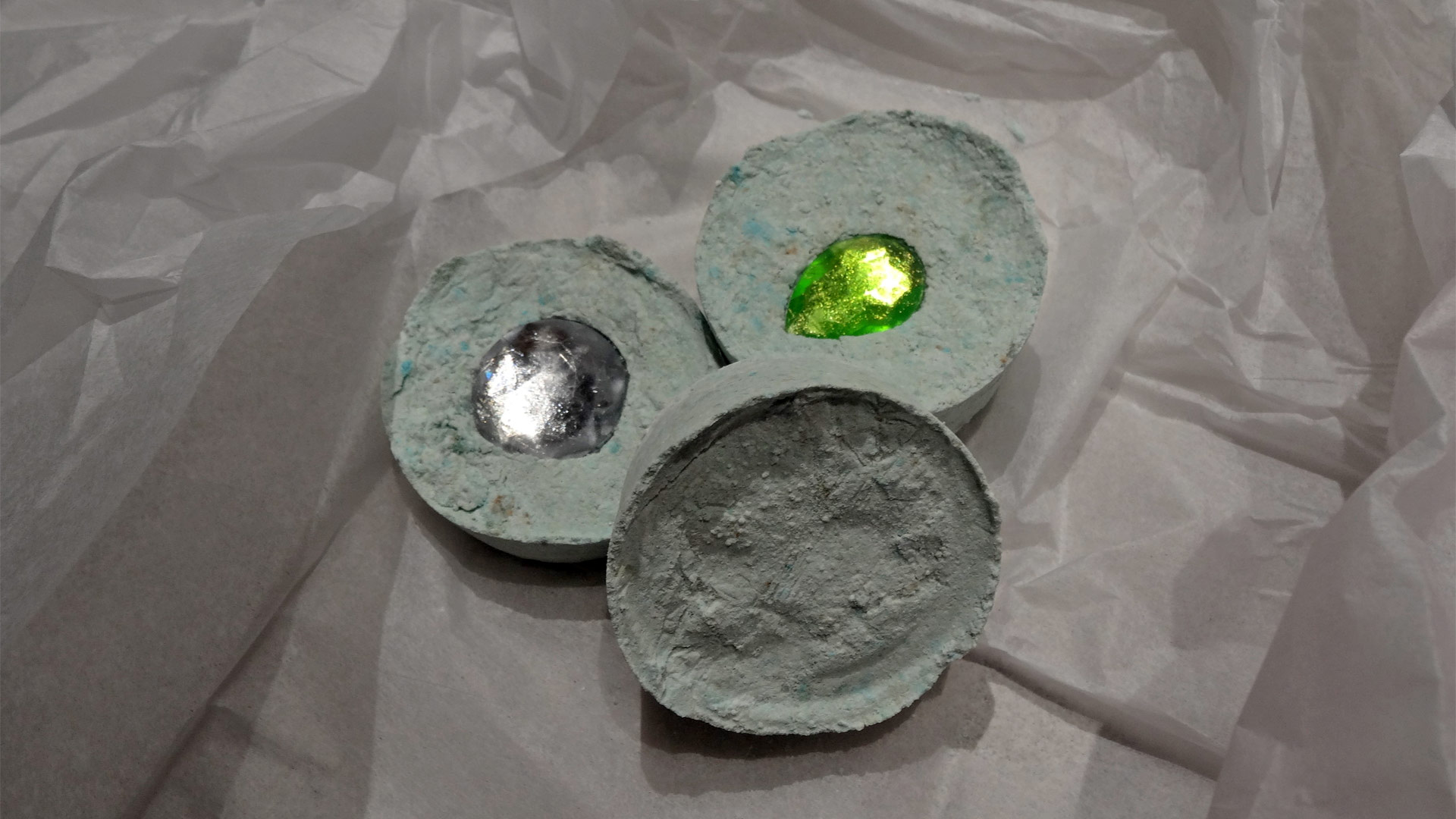 Three handmade soap discs in the shape of hockey pucks, with a single embedded silver and emerald jewel