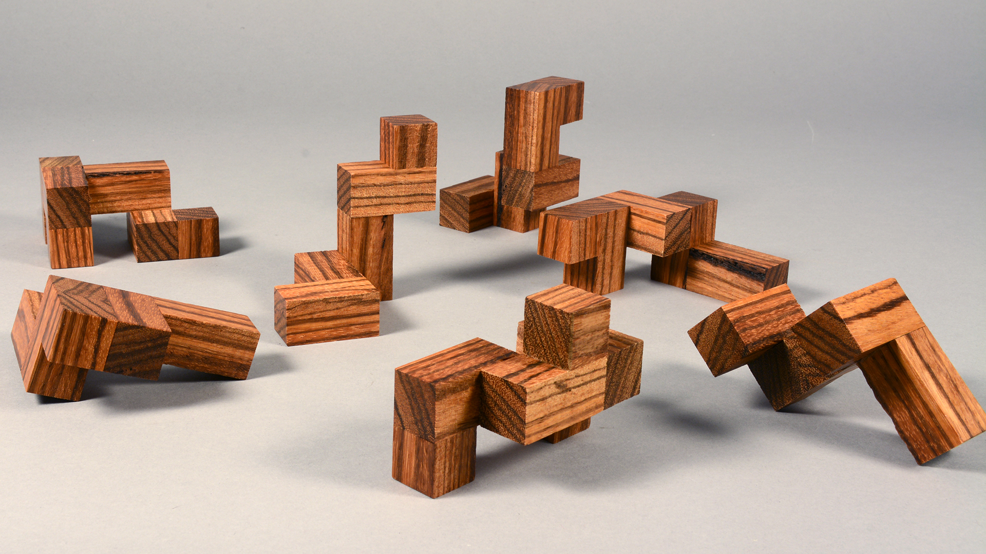 Stained wood 3D geometric interlocking puzzle pieces scattered about