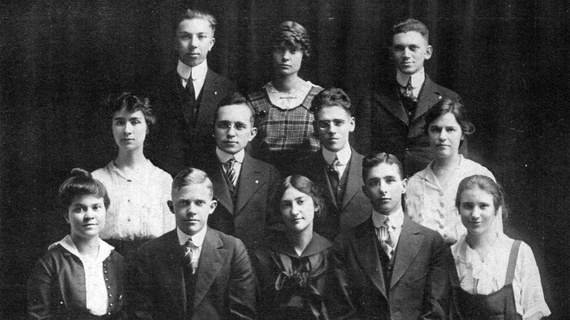 Early 20th century yearbook photo. 12 men and women in formal dress pose in a portrait style.