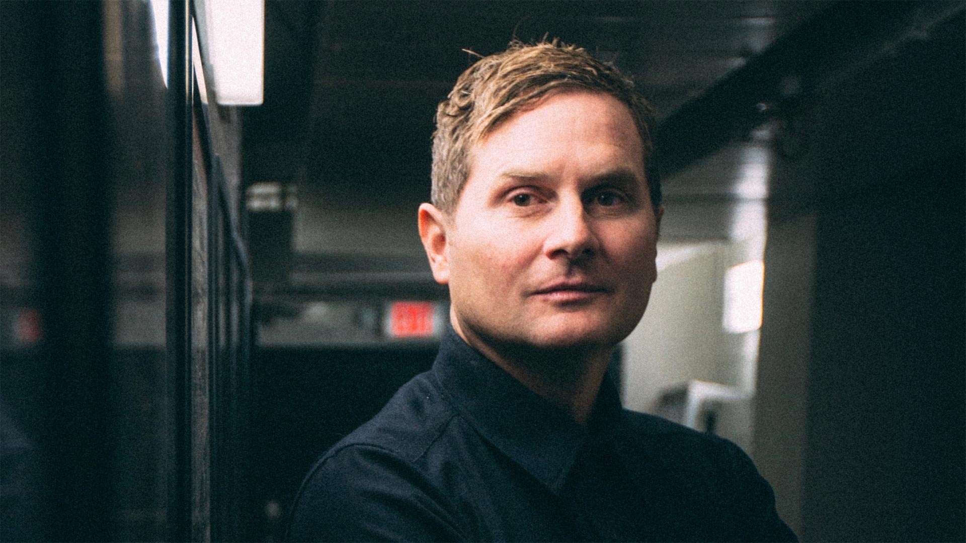 headshot of a man in a dark hallway or backstage area