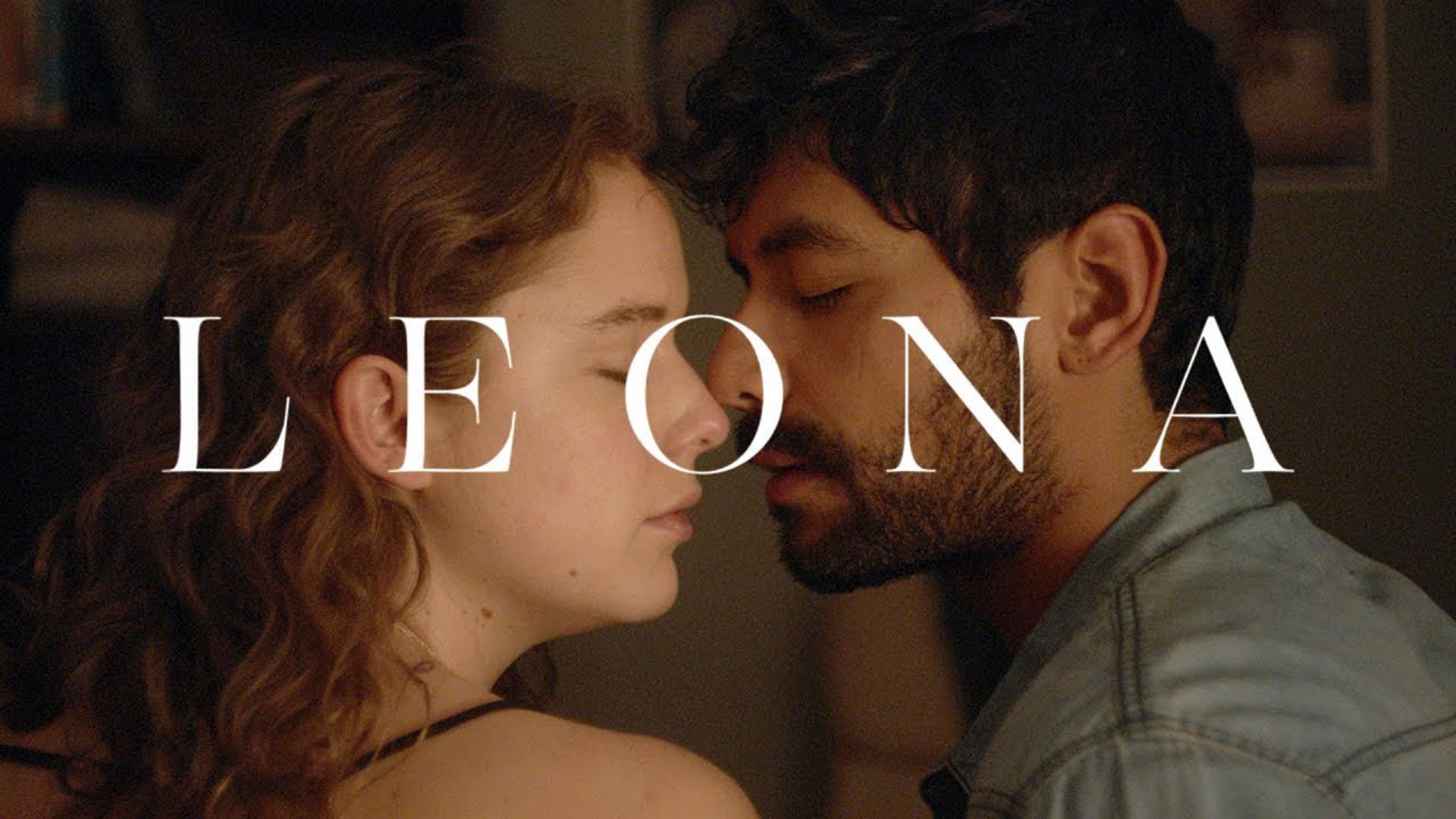 Woman and man about to kiss with noses touching. Leona in text on top in white font.