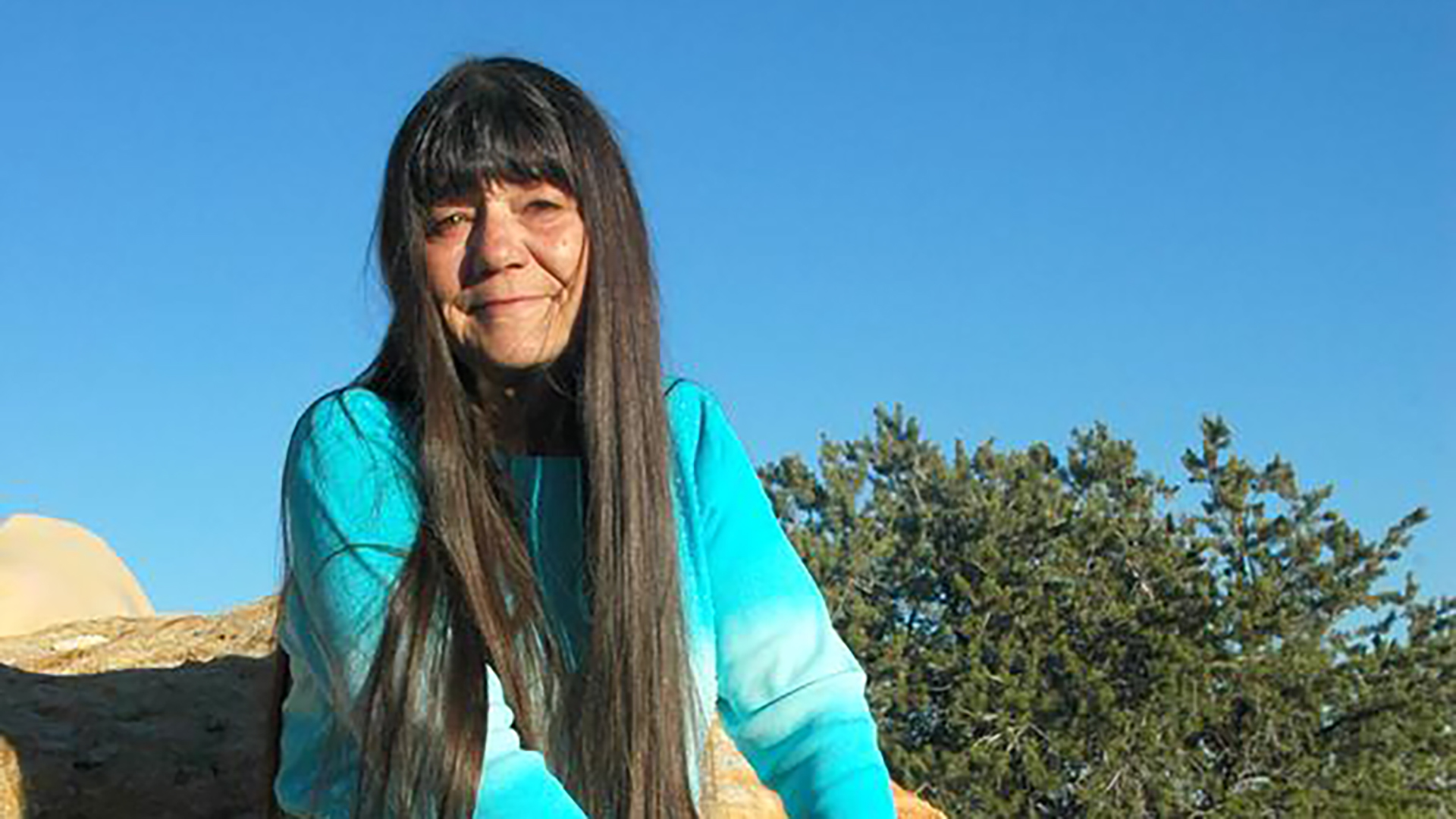 female storyteller wearing light blue sitting on a rock outside