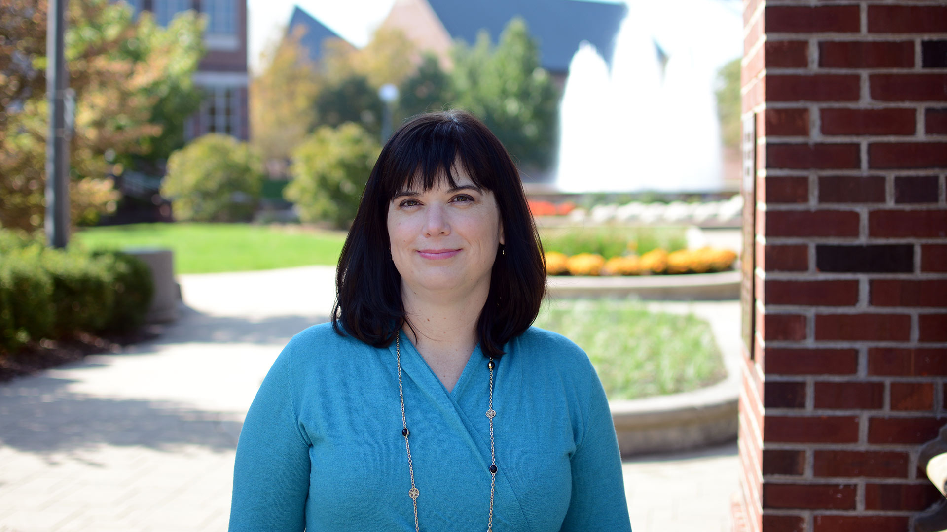 Elizabeth Sutton stands outside in front of a sunny plaza with fountain and museum in the background