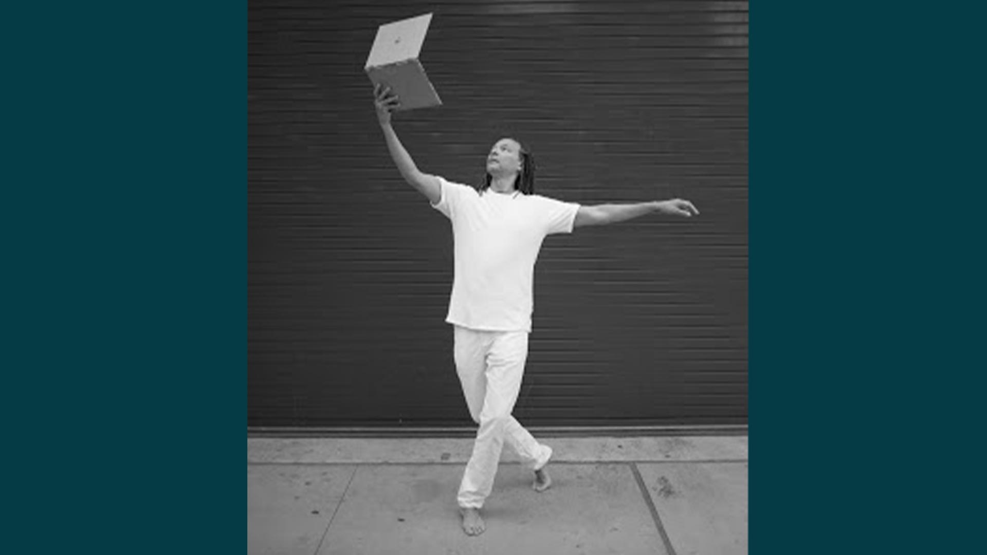 image of Thomas DeFrantz in a dance pose with a laptop in one hand extended above his head