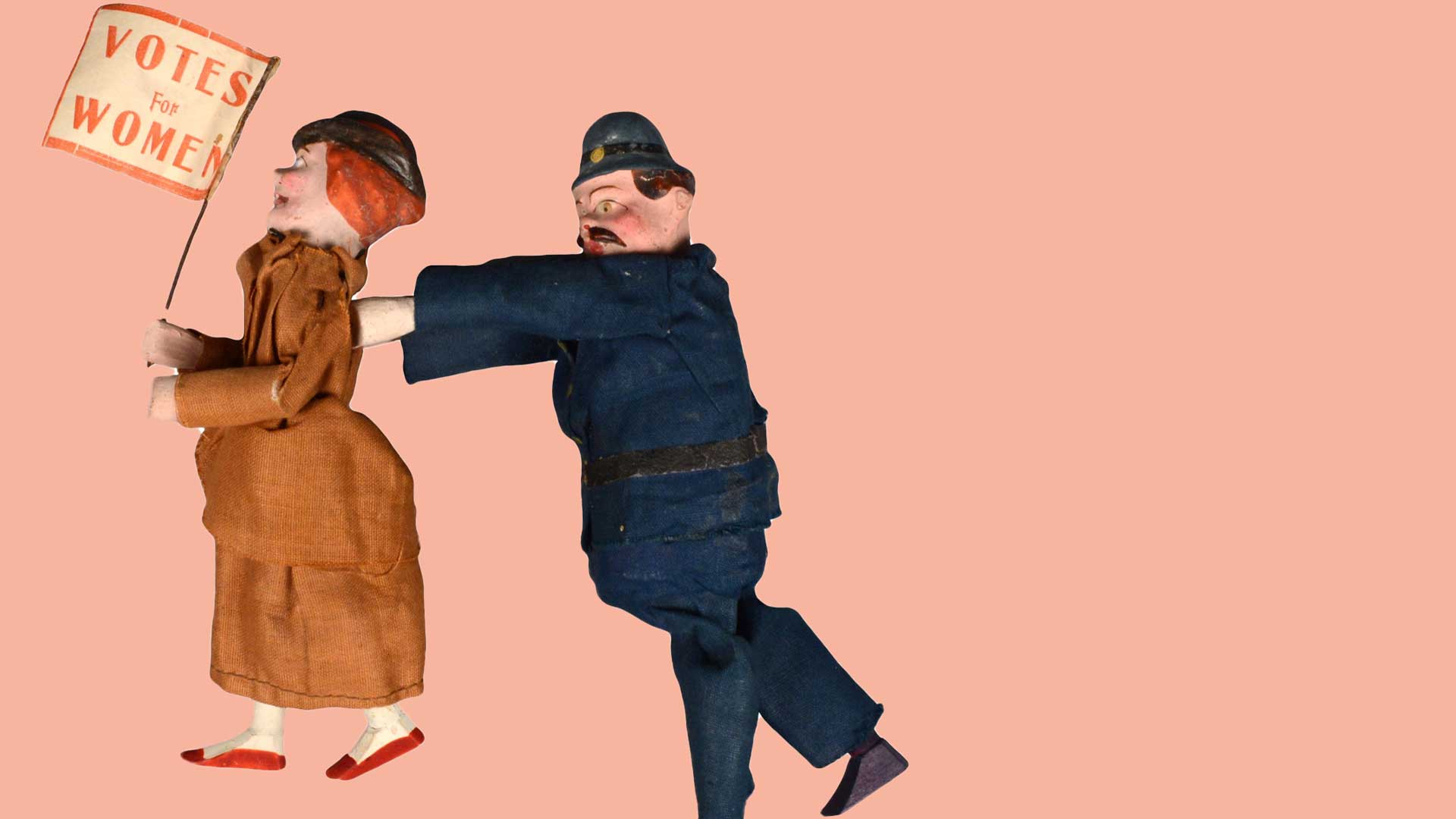 one woman doll holding a sign saying "Votes for Women" being pushed by a police officer doll