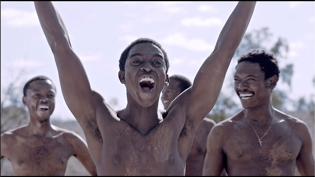 4 shirtless men laughing with one man extending his arms up in a "V"