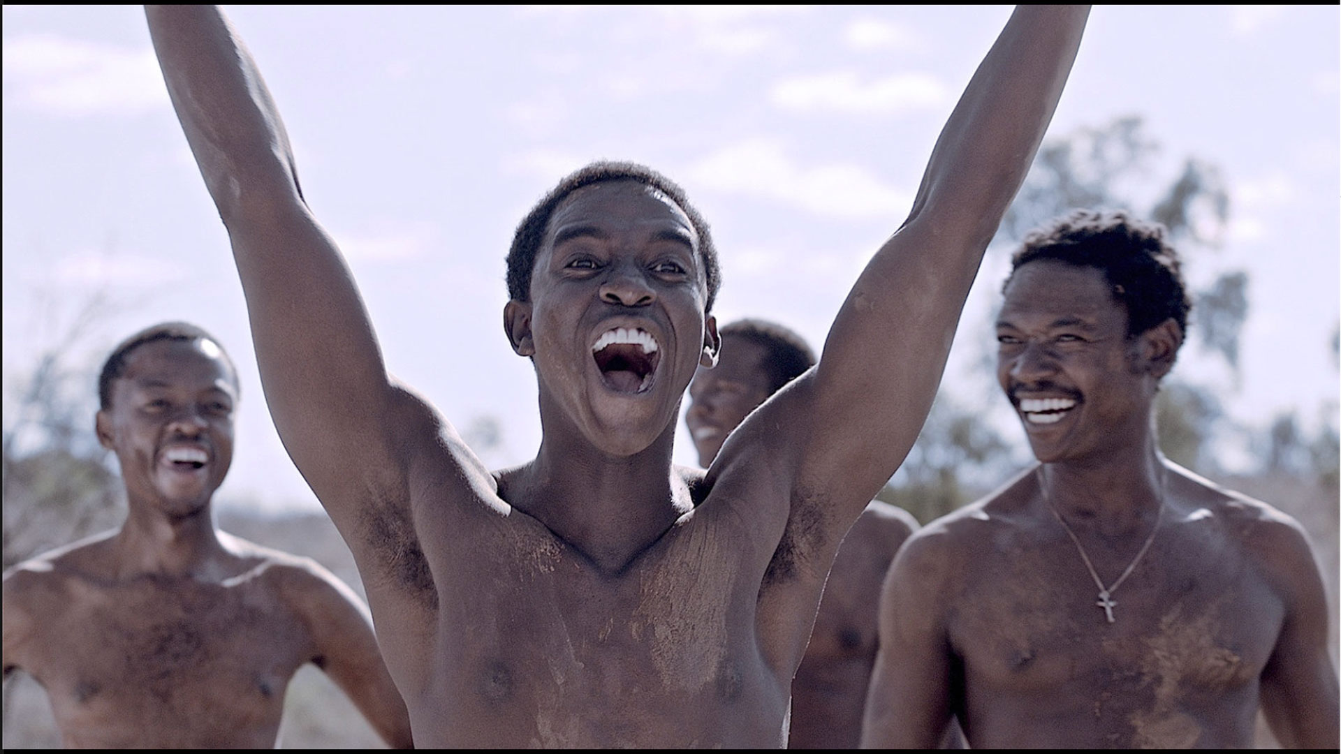 4 shirtless men laughing with one man extending his arms up in a 