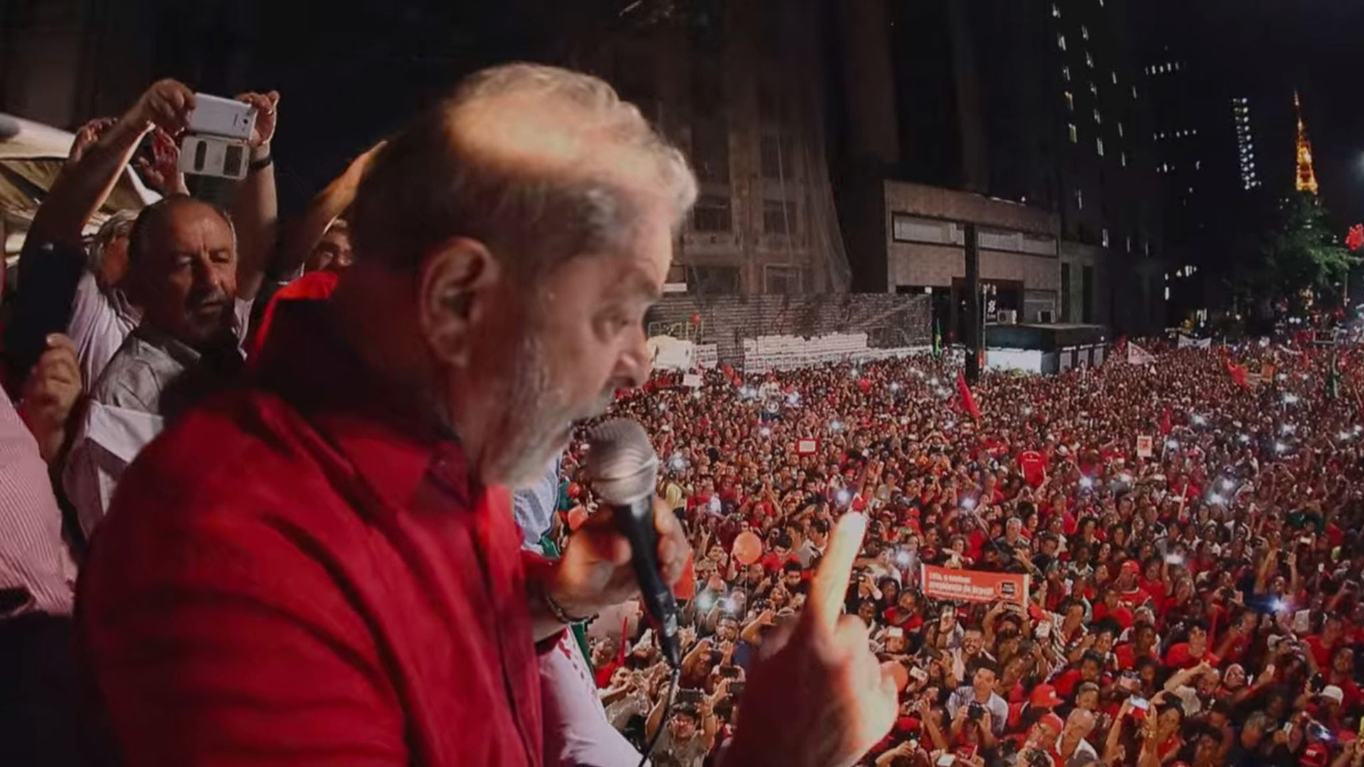 An older man speaks at a very large crowd