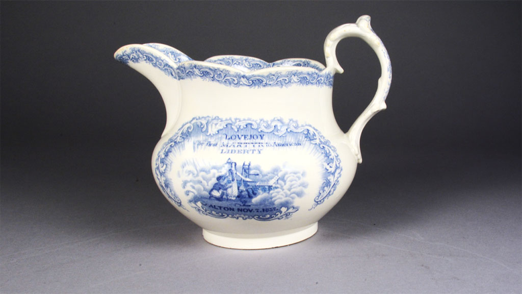 White pitcher with blue design that reads "Lovejoy, the first martyr to American liberty".