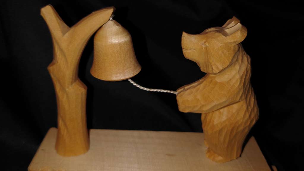 small scene of a wooden bear pulling a wooden bell on a wooden tree