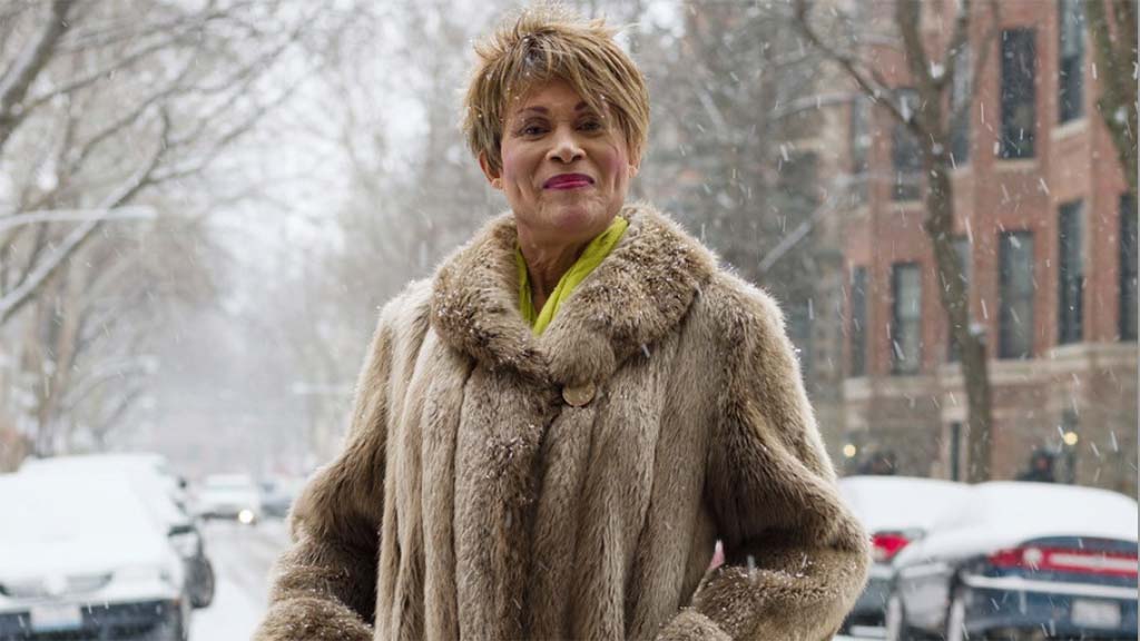 Person wearing a fur coat poses proudly in the street of a city's residential district in the snow