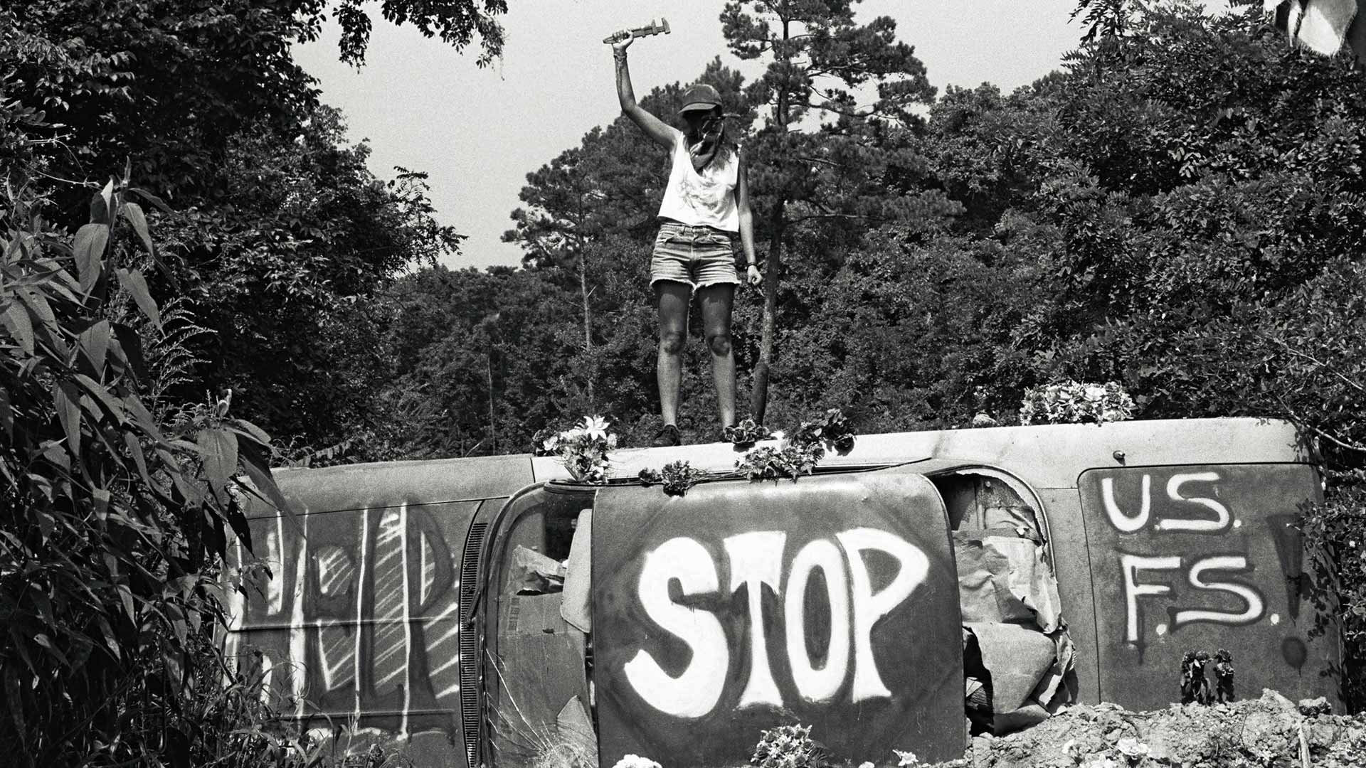 Greyscale picture of an activist standing on a tilted car with the words 