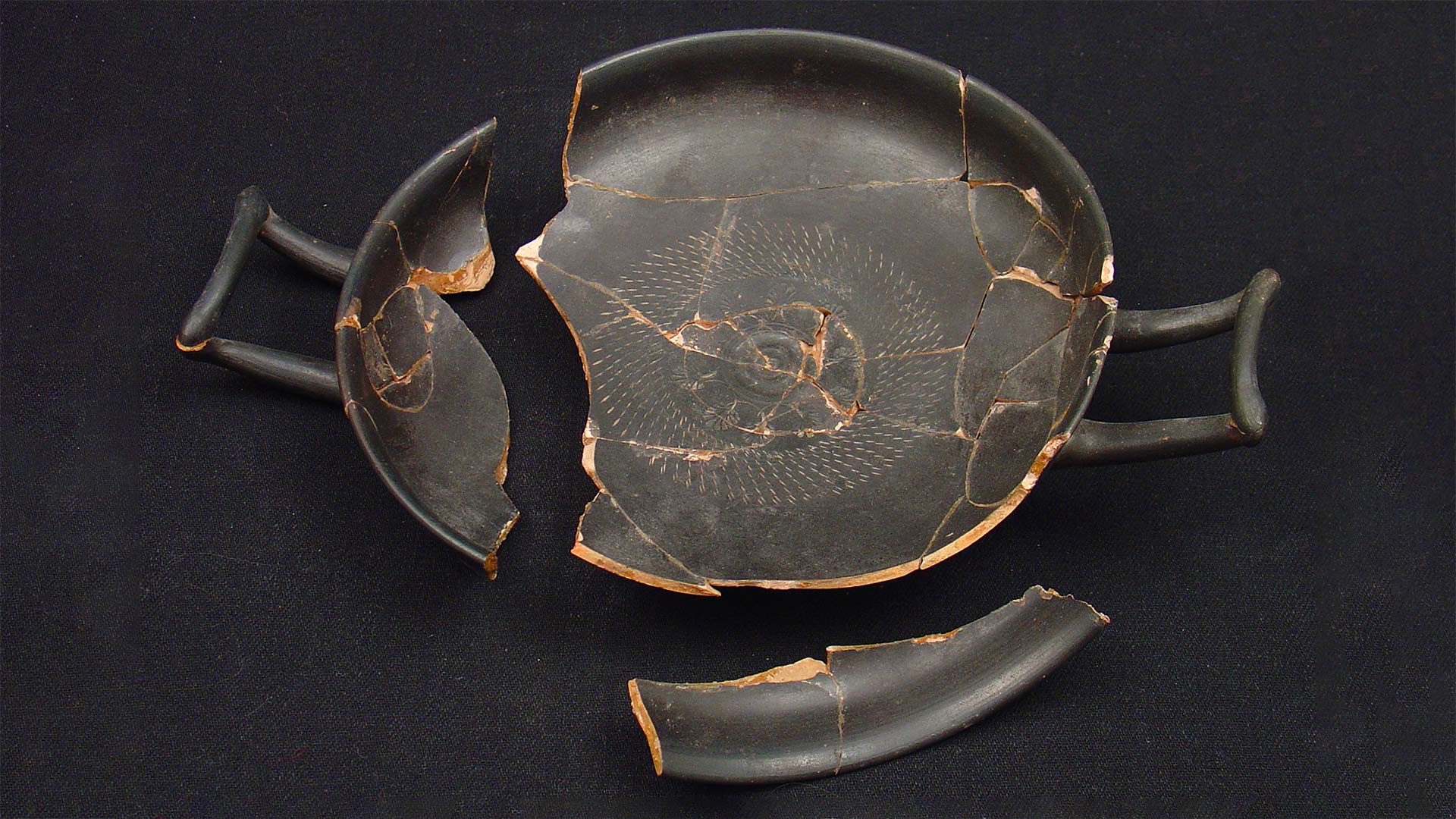 A fragmented black and gold shallow drinking cup from the Hellenistic Italian period.