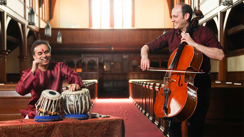 Color image of Sandeep Das playing the tabla, an Indian drum, on the left and Mike Block playing the cello on the right.