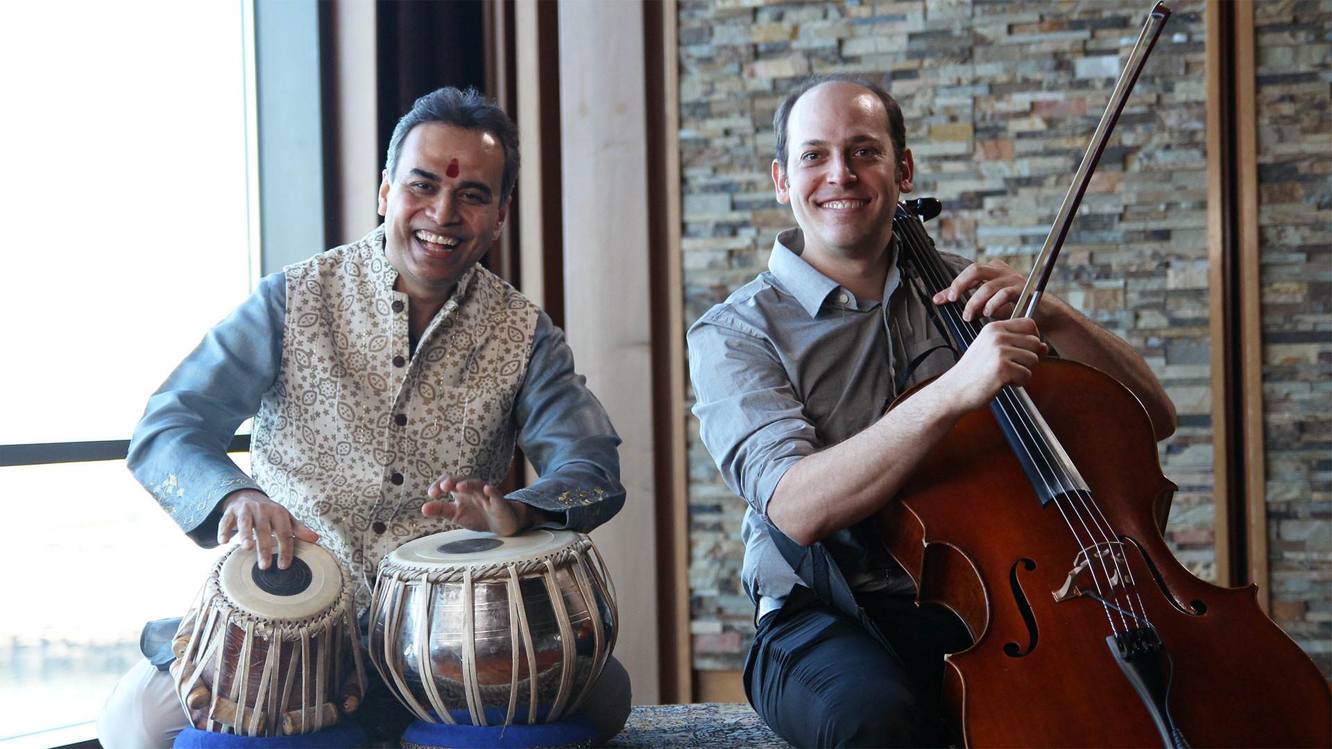 Color image of Sandeep Das playing the tabla, an Indian drum, on the left and Mike Block playing the cello on the right.