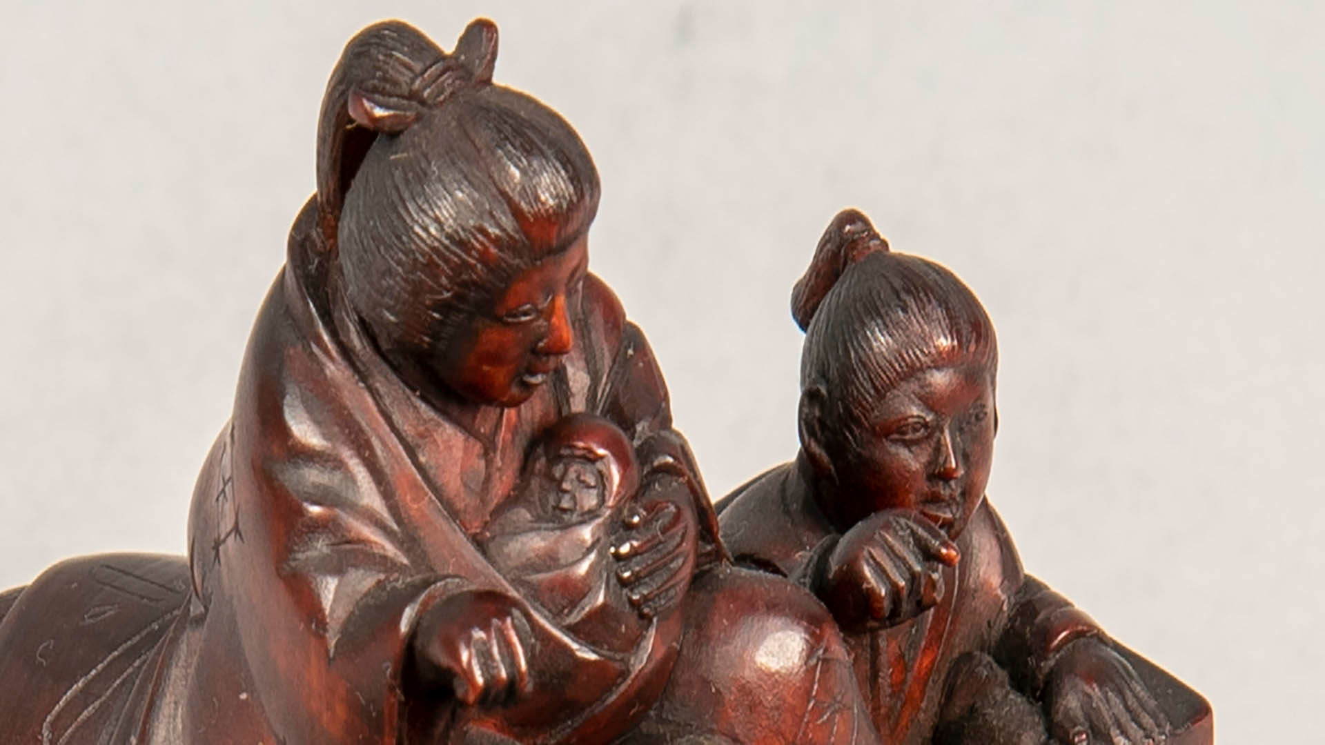 red japanese sculpture of a mother cradling a newborn baby, an older child is sitting next to her