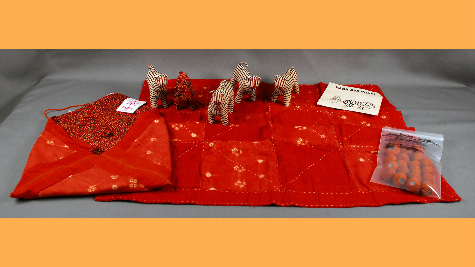 an artifact photo of a game with red fabric, tiger figurines, pouch, and a bag of red beads