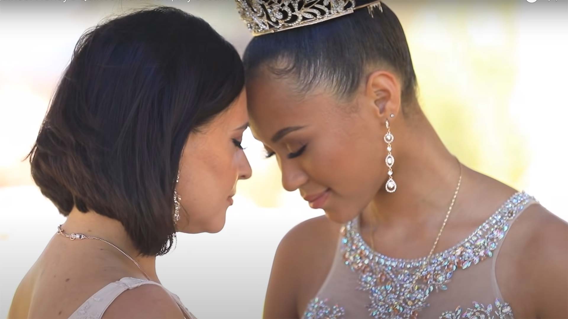 smiling young woman with closed eyes and tiara leans forehead another womans forehead